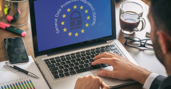 Manos sobre un teclado de laptop y el logo de GDPR en la pantalla