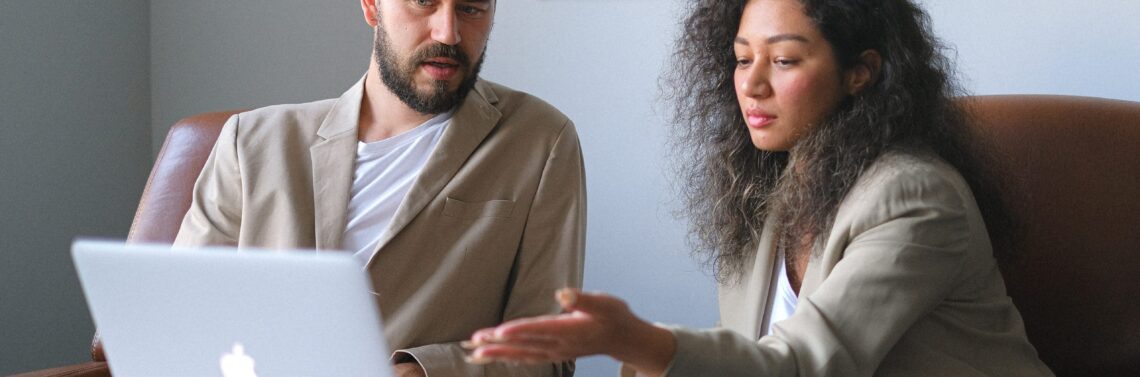 Una mujer y un hombre conversan sobre por qué contratar a una empresa de outsourcing IT mientras miran una laptop