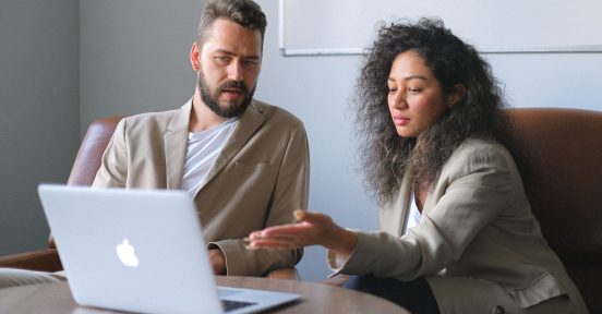 A woman and a man discuss why to hire an IT outsourcing company while looking at a laptop