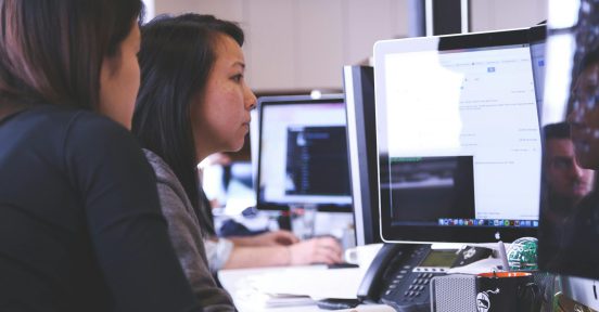 dos mujeres miran un monitor mientras realizan tareas usando IA